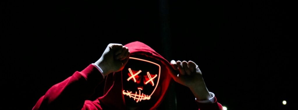 A spooky illuminated mask figure with a red hoodie in a dark setting, perfect for Halloween themes.