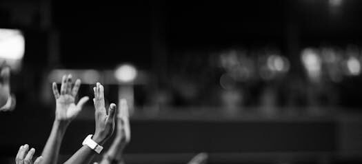 Black and white image of audience with hands raised, capturing concert energy.